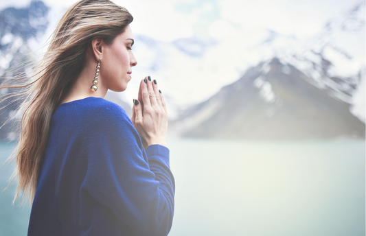 A woman praying near mountains.