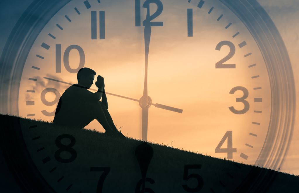 A man praying in front of a large clock.