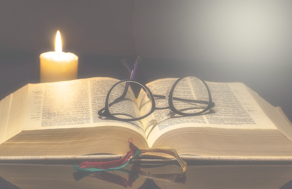 Open Bible with candle and glasses on top.