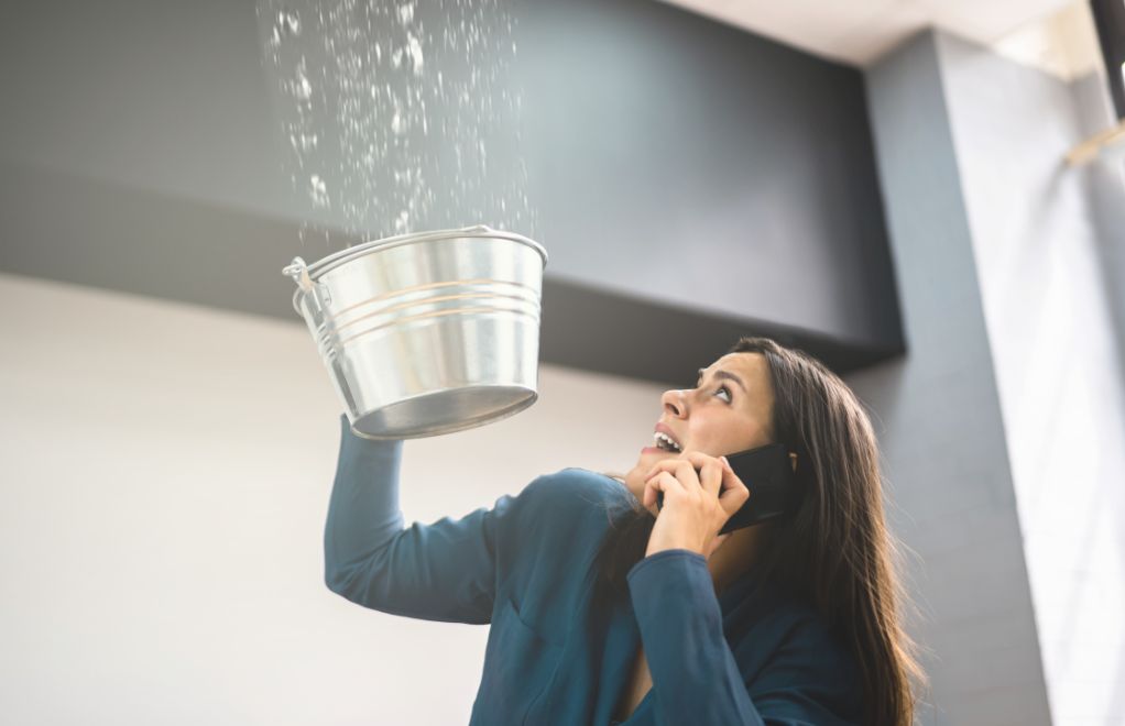 Woman catching water leak in a bucket.