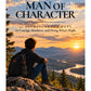 Book cover for 'A Man of Character: 31 Devotions for Boys on Courage, Kindness, and Doing What's Right' by Jamee Leigh, featuring a young man sitting on a rock overlooking a mountain landscape at sunset.